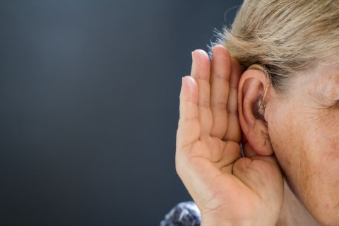 Persoon met gehoorapparaat luistert aandachtig, beeld voor hoe tinnitus en gehoorverlies samenhangen