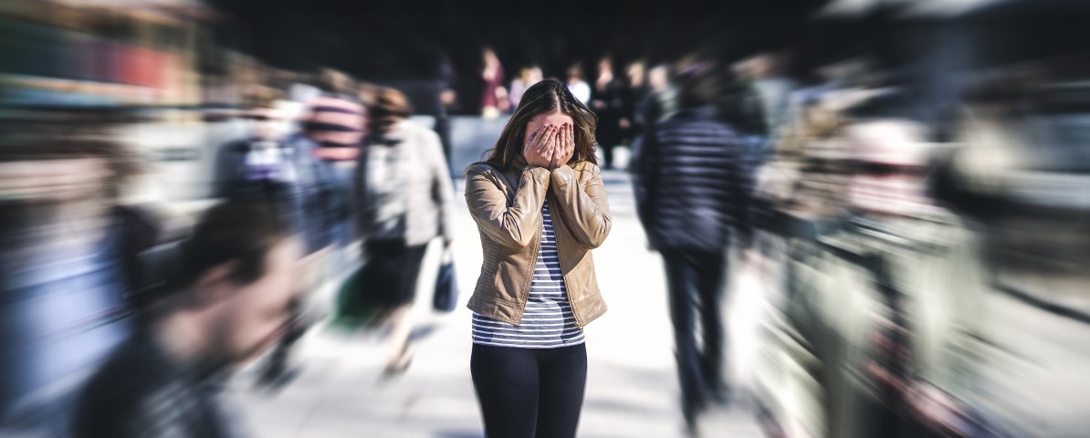 Persoon staat angstig in drukke menigte, beeld voor hoe tinnitus angst en overprikkeling kan versterken.
