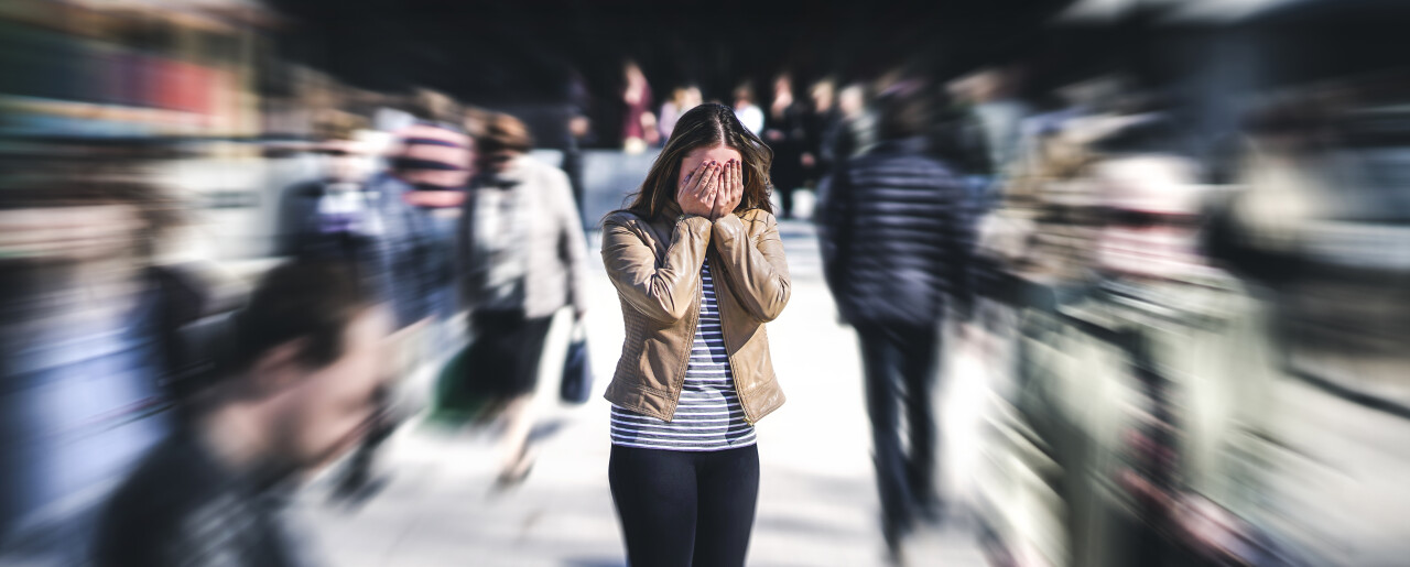 Persoon staat angstig in drukke menigte, beeld voor hoe tinnitus angst en overprikkeling kan versterken.